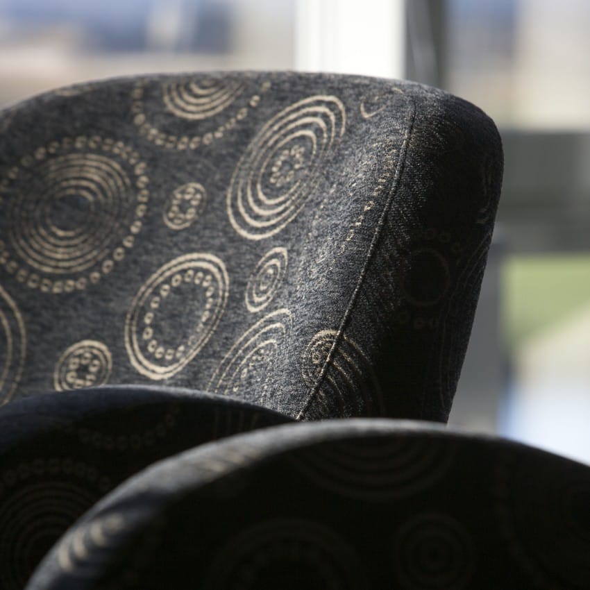 Nærbilde av en mønstret svart stol med sirkulære design foran et mykt opplyst vindu. Foto: Nathan Lediard, Lediard Foto AS.