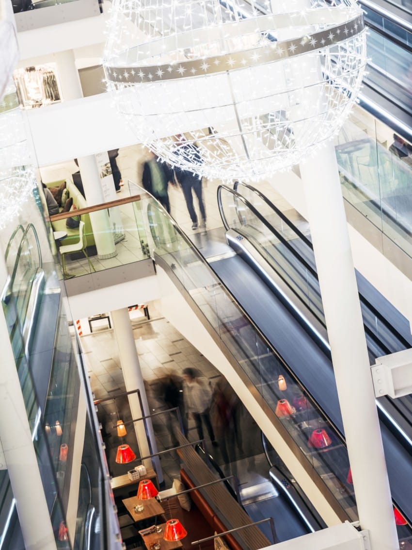Moderne kjøpesenterinteriør med flere nivåer med rulletrapper, glassrekkverk og store sfæriske lysarmaturer. Foto: Nathan Lediard, Lediard Foto AS.