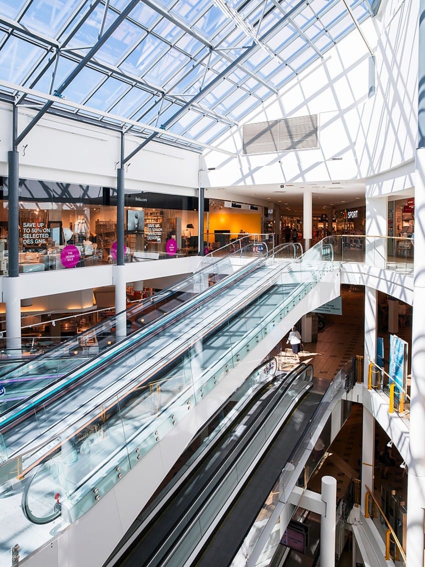 Romslig kjøpesenterinteriør med solrikt takvindu, rulletrapper og ulike utstillingsvinduer. Foto: Nathan Lediard, Lediard Foto AS.
