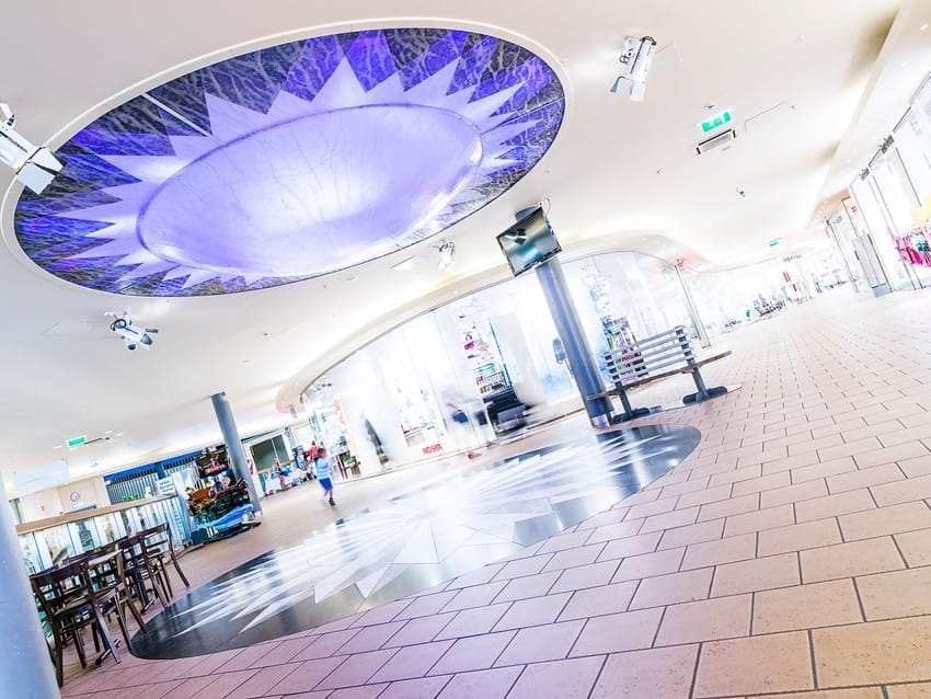 Romslig, moderne atrium med geometriske mønstre i tak og gulv, med bord og en sentral søyle. Foto: Nathan Lediard, Lediard Foto AS.