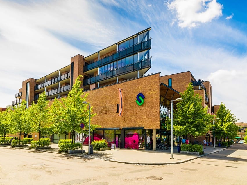 Moderne murbygning med store vinduer, fargerik logo, grønne trær og en livlig rosa skulptur utenfor. Foto: Nathan Lediard, Lediard Foto AS.