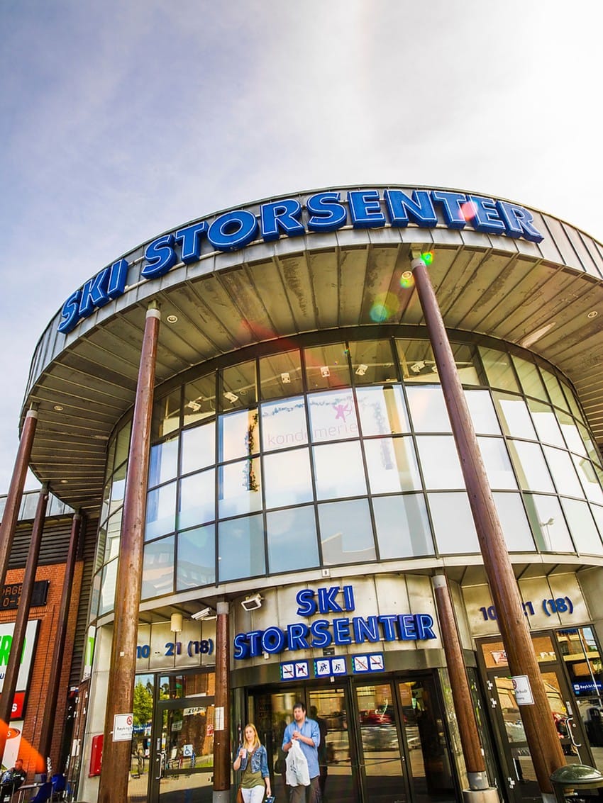 Inngang til Ski Storsenter med stor glassfasade, trestolper, og folk som går foran. Foto: Nathan Lediard, Lediard Foto AS.