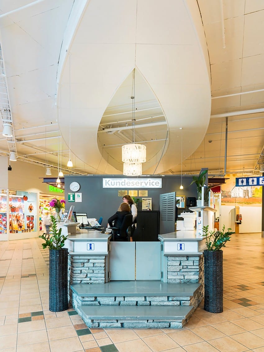 Kundeservice i et kjøpesenter med dråpeformet takdesign og en person som sitter ved disken. Foto: Nathan Lediard, Lediard Foto AS.