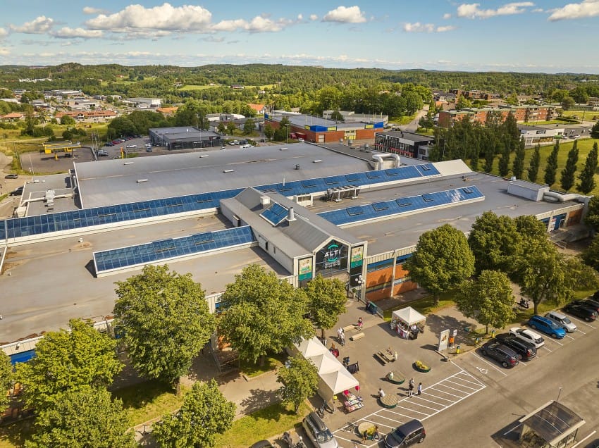 Luftfoto av et stort kjøpesenter med solcellepaneler, omgitt av parkeringsplasser og grøntområder. Foto: Nathan Lediard, Lediard Foto AS.