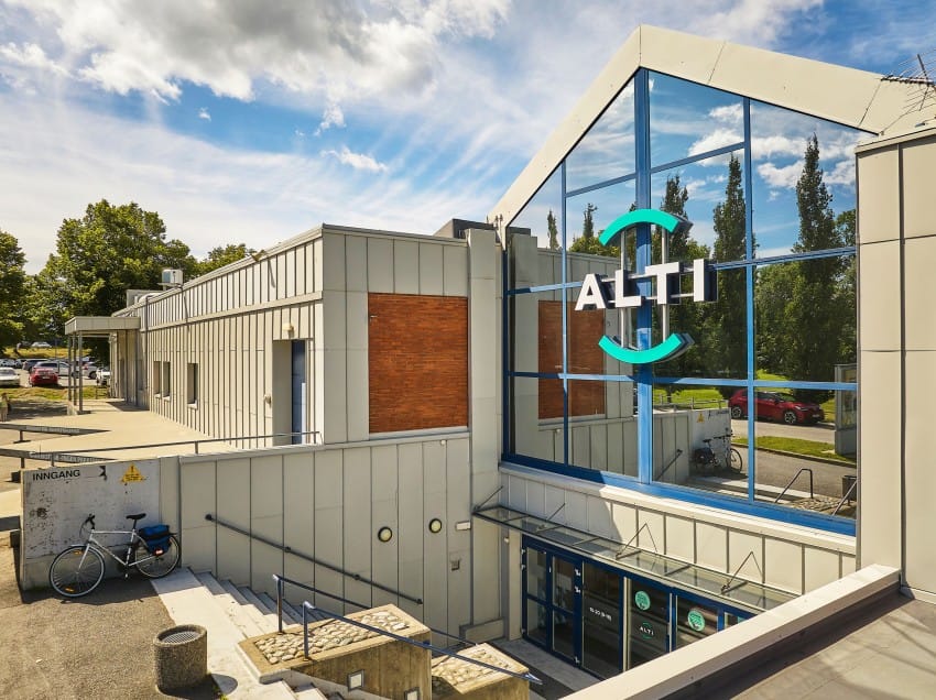 Moderne bygg med store glassvinduer og "ALTI"-skilt, trapp til inngang, og en parkert sykkel. Foto: Nathan Lediard, Lediard Foto AS.
