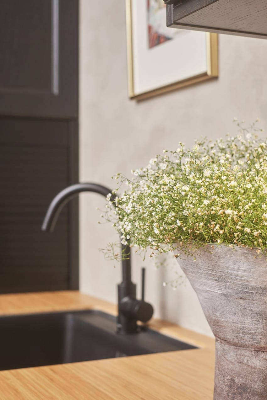 Vase med hvite blomster nær en kjøkkenvask med en svart kran på en benkeplate i tre. Foto: Nathan Lediard, Lediard Foto AS.