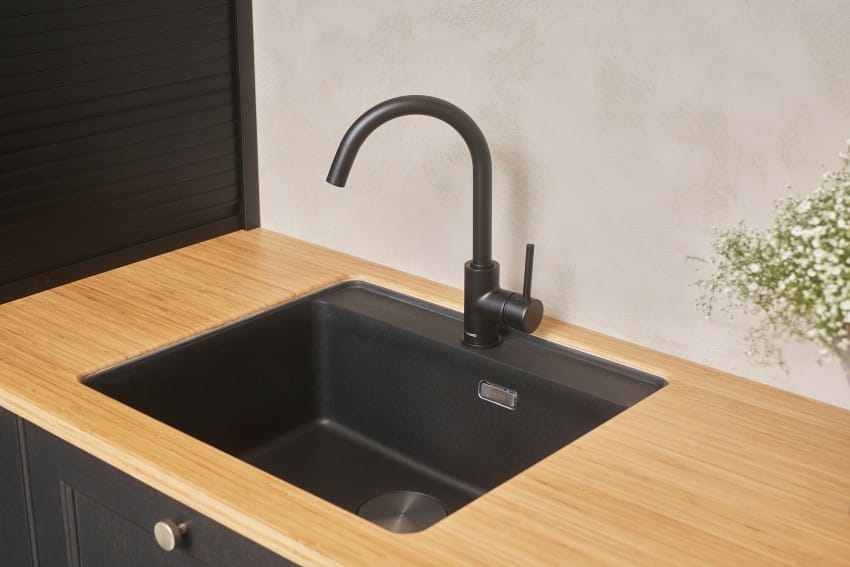 Moderne kjøkkenvask med sort armatur, satt i benkeplate i tre. En liten plante er delvis synlig til høyre. Foto: Nathan Lediard, Lediard Foto AS.