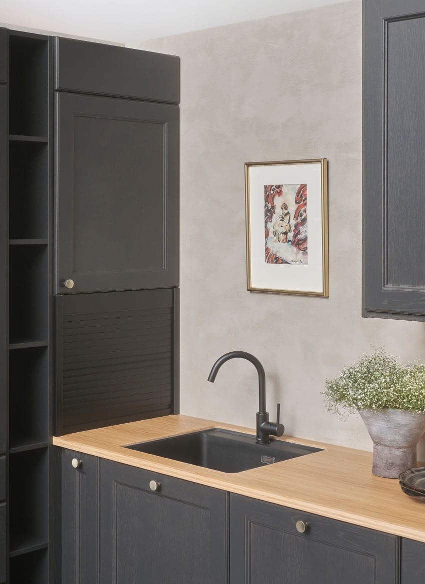 Moderne kjøkken med mørke skap, benkeplate i tre og svart vask. Innrammet kunst og blomster dekorerer veggen. Foto: Nathan Lediard, Lediard Foto AS.