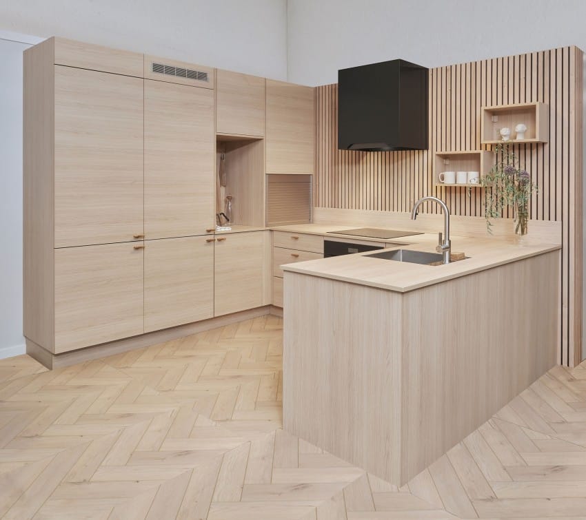 Moderne kjøkken med lyse treskap, øy, fiskebeinsgulv og svarte detaljer. Vertikale lameller gir tekstur. Foto: Nathan Lediard, Lediard Foto AS.