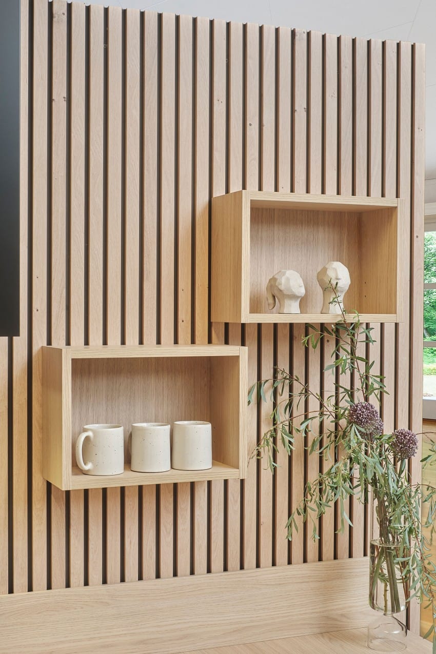 Trehyller på en spaltevegg med krus, skulpturer og en vase med blomster og grønt. Foto: Nathan Lediard, Lediard Foto AS.