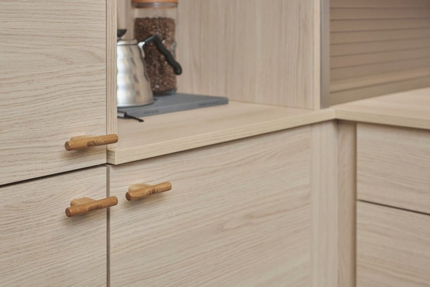 Kjøkkenskap i lyst tre med enkle trehåndtak og en vannkoker i metall på benken. Foto: Nathan Lediard, Lediard Foto AS.