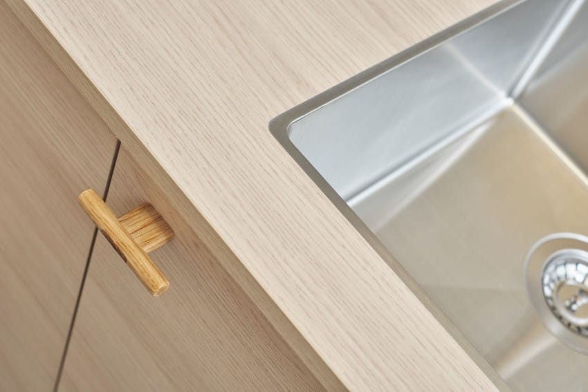 Nærbilde av en moderne kjøkkenvask med et lyst treskap og et metallhåndtak. Foto: Nathan Lediard, Lediard Foto AS.