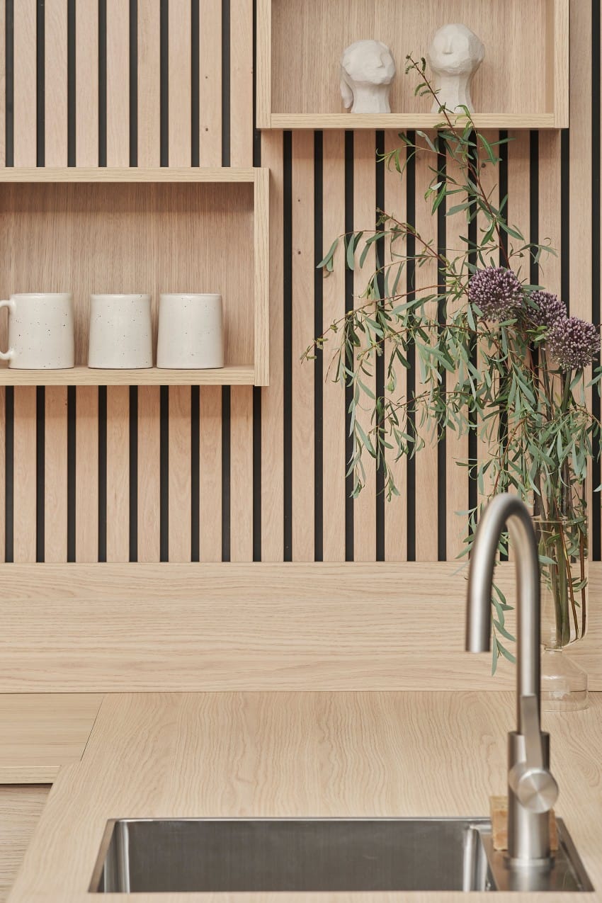 Moderne kjøkken med trehyller, krus, veggdekor og en metallkran med blomster i en vase. Foto: Nathan Lediard, Lediard Foto AS.