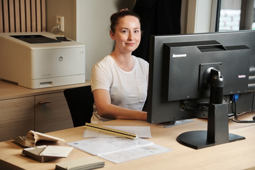 Person i hvit skjorte som sitter ved et skrivebord med en datamaskin, papirer og en skriver i bakgrunnen. Foto: Nathan Lediard, Lediard Foto AS.