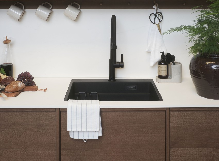Moderne kjøkkenvask med svart kran, treskap og tilbehør til benkeplater, inkludert kopper og kjøkkenhåndkle. Foto: Nathan Lediard, Lediard Foto AS.