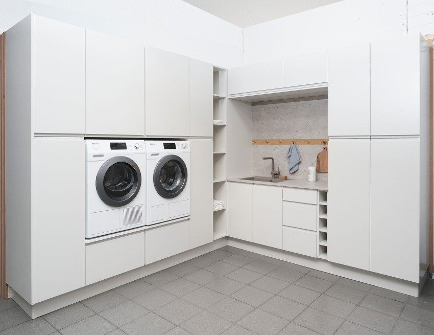 Moderne vaskerom med hvite skap, vaskemaskin, tørketrommel og benkeplate med vask. Grå fliser på gulv. Foto: Nathan Lediard, Lediard Foto AS.