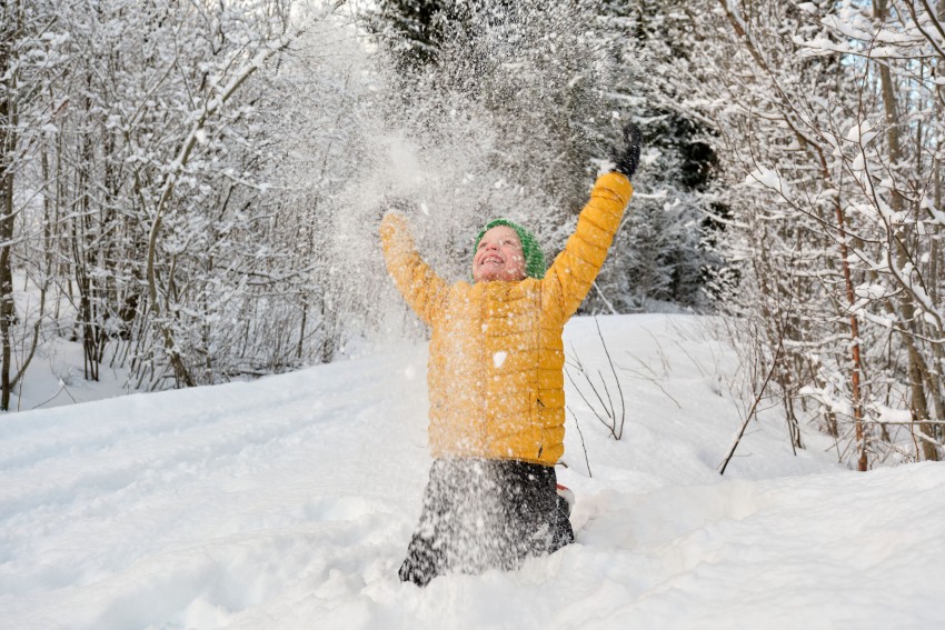 Person i gul jakke som kneler i snø, gledeskastende snø opp i luften, omgitt av snødekte trær. Foto: Nathan Lediard, Lediard Foto AS.