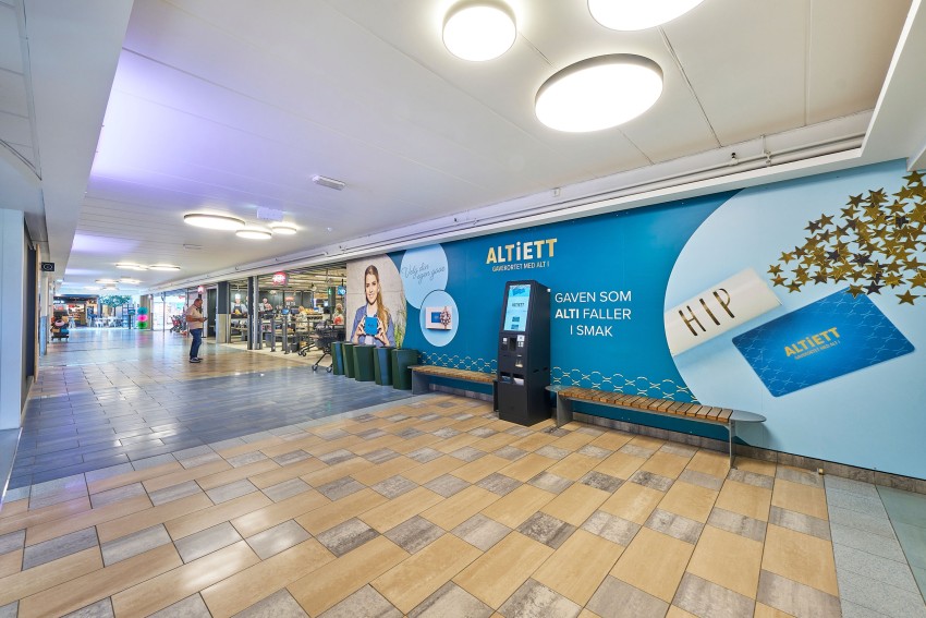 Kjøpesenterkorridor med salgsfremmende veggutstillinger, benk og en salgsautomat. Foto: Nathan Lediard, Lediard Foto AS.