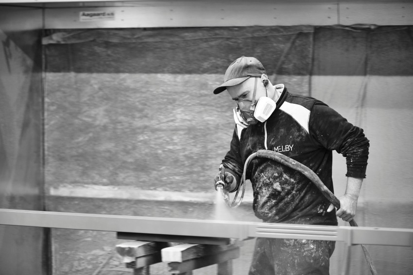En arbeider i en maske som bruker en spraymalingspistol på en metallramme i et verksted. Foto: Nathan Lediard, Lediard Foto AS.