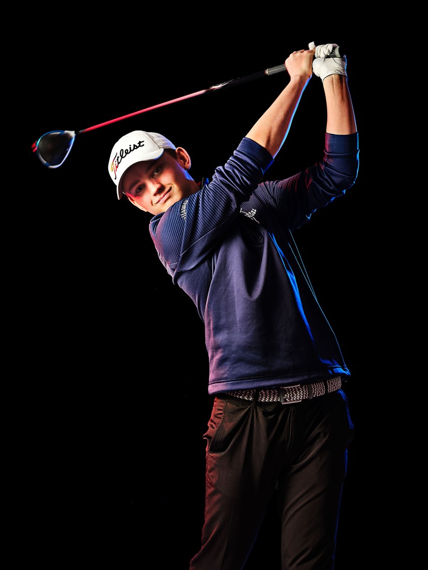 Person i blå genser og hatt svinger en golfkølle mot en svart bakgrunn. Foto: Nathan Lediard, Lediard Foto AS.