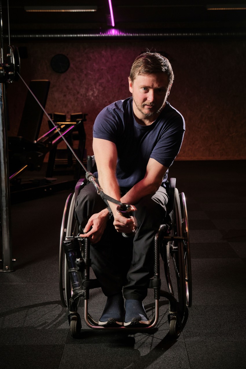 Person i rullestol som trener med motstandskabler i et svakt opplyst treningsstudio. Foto: Nathan Lediard, Lediard Foto AS.