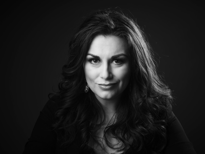 Kvinne med langt bølget hår og øredobber, smilende lett, i et svart-hvitt portrett. Foto: Nathan Lediard, Lediard Foto AS.
