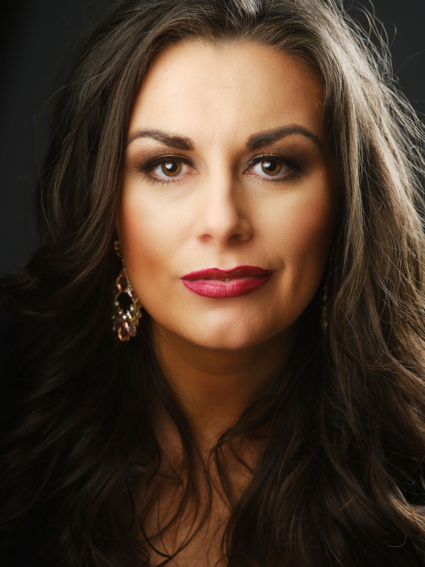 Kvinne med langt, mørkt bølget hår, iført øredobber og rød leppestift, ser direkte på kameraet. Foto: Nathan Lediard, Lediard Foto AS.