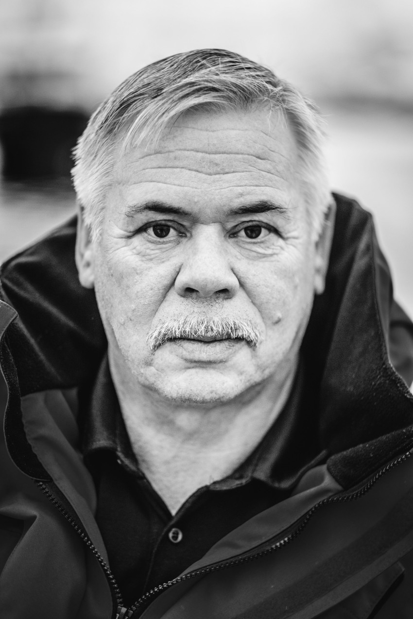 Svart-hvitt portrett av en mann med bart, iført en mørk jakke, og ser direkte på kameraet. Foto: Nathan Lediard, Lediard Foto AS.