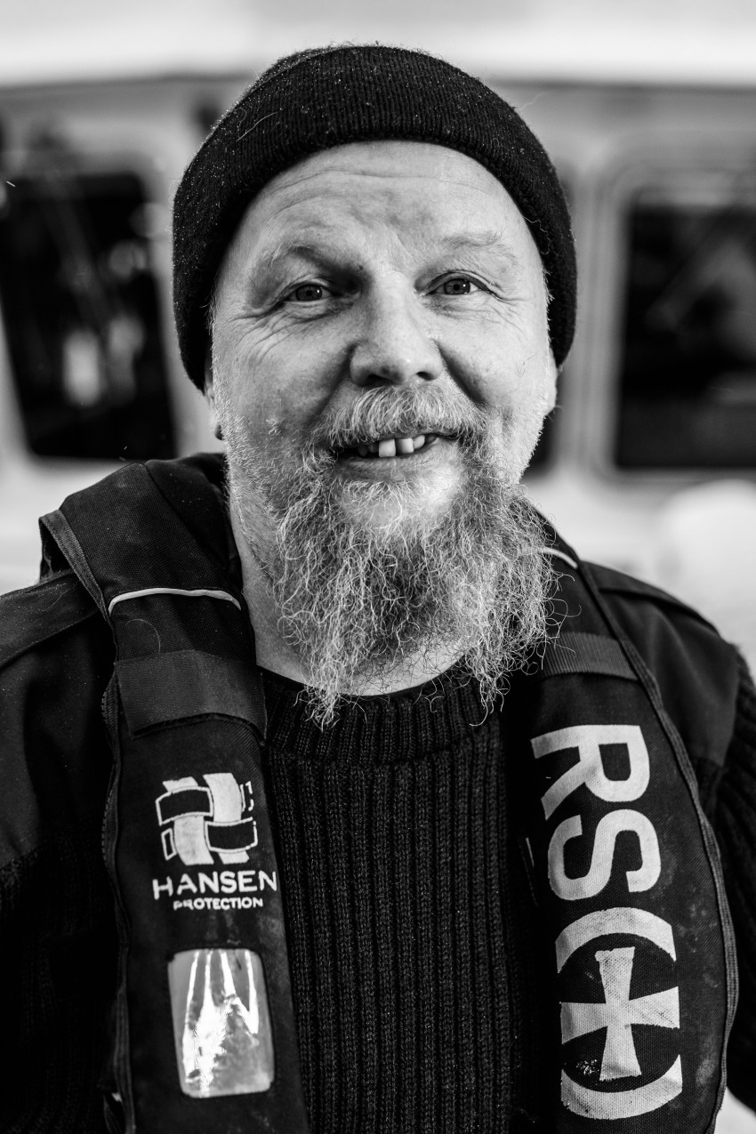 En skjeggete mann iført lue og redningsvest smiler varmt til kameraet. Foto: Nathan Lediard, Lediard Foto AS.