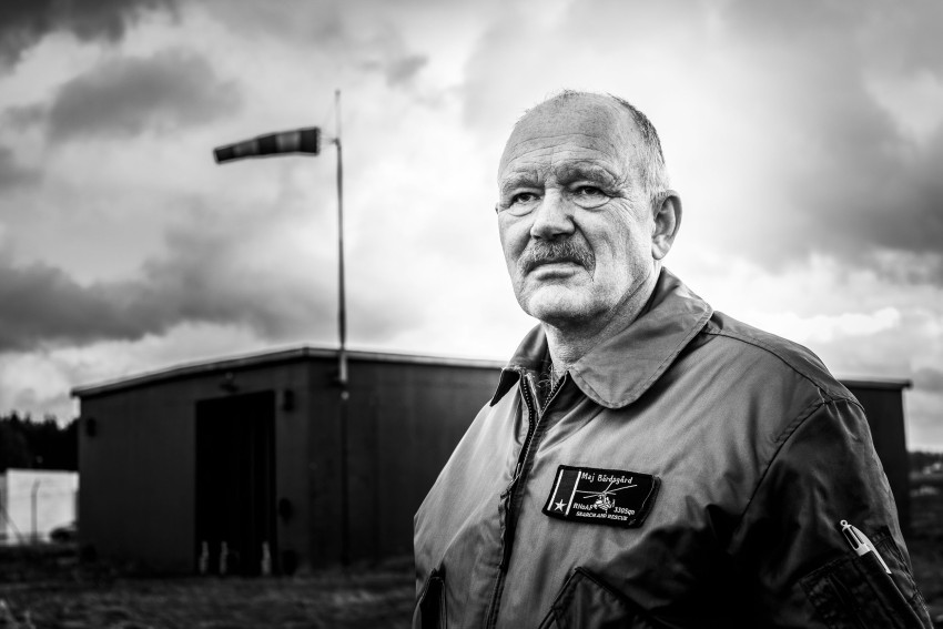 Mann i flyjakke står utenfor nær en vindsokk og bygger under overskyet himmel. Foto: Nathan Lediard, Lediard Foto AS.