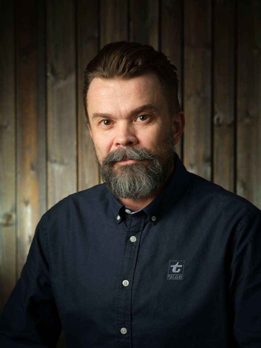 Mann med skjegg i mørk skjorte mot trebakgrunn. Foto: Nathan Lediard, Lediard Foto AS.