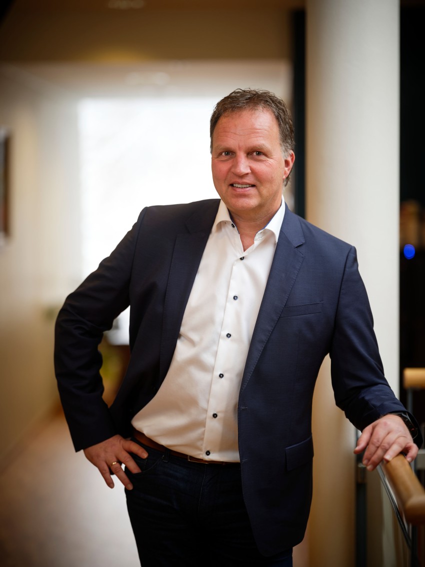 En mann i dress står i en gang, lent på et rekkverk, med et selvsikkert uttrykk. Foto: Nathan Lediard, Lediard Foto AS.