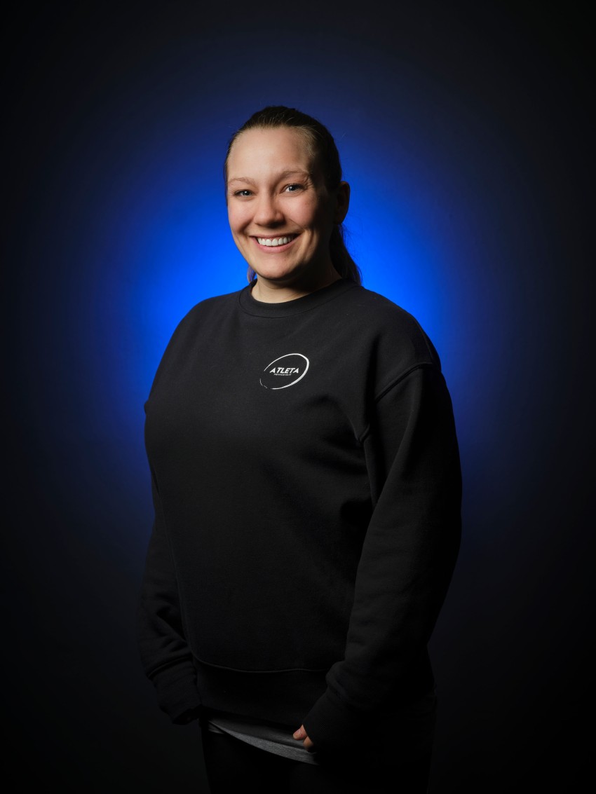 Smilende person i en svart genser med blå gradientbakgrunn. Foto: Nathan Lediard, Lediard Foto AS.