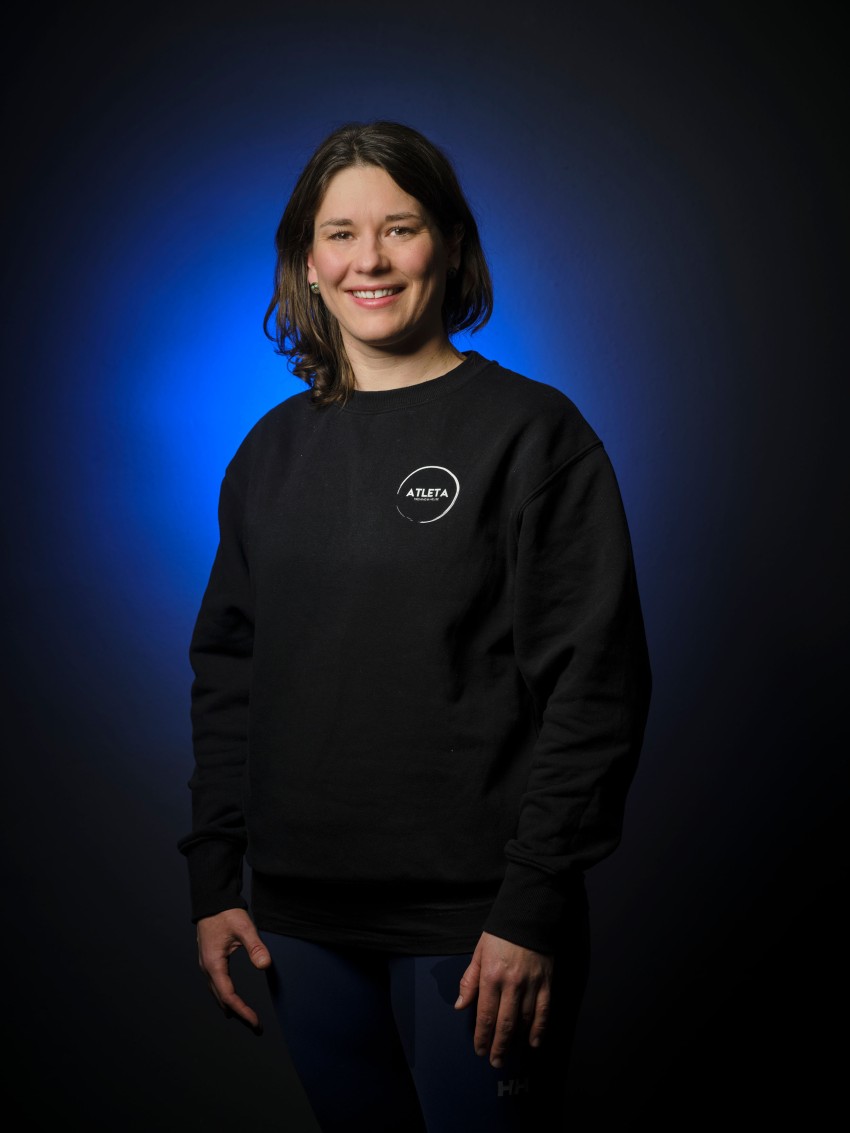 Smilende kvinne i en svart sweatshirt står mot en blå og svart gradientbakgrunn. Foto: Nathan Lediard, Lediard Foto AS.