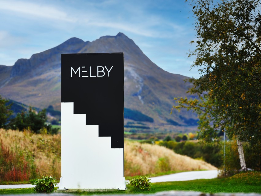 Skilt som sier «MELBY» mot et fjellandskap med overskyet himmel og gressletter. Foto: Nathan Lediard, Lediard Foto AS.