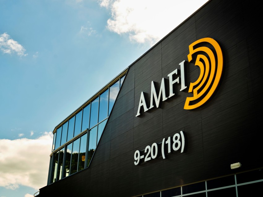 Bygning med "AMFI"-logo og gult ikon på mørk vegg, satt mot en blå himmel og skyer. Foto: Nathan Lediard, Lediard Foto AS.