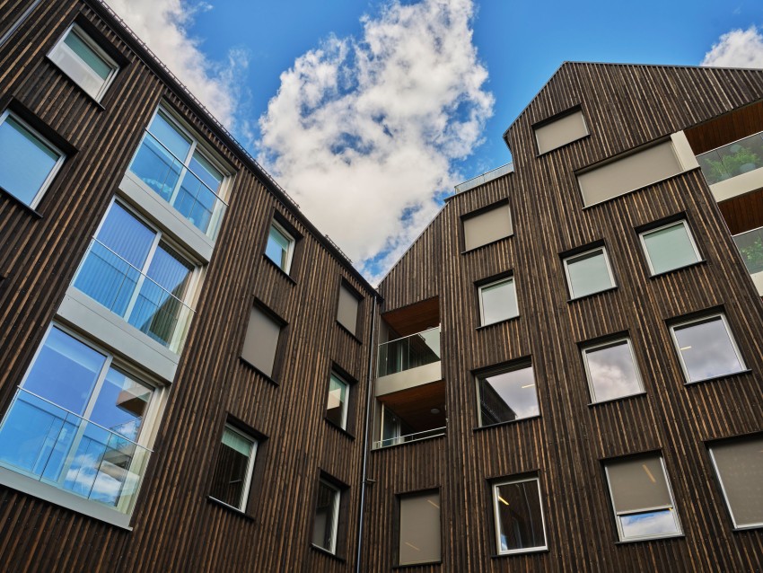 Trekledde moderne bygninger under en blå himmel med spredte skyer, sett nedenfra i et vinklet perspektiv. Foto: Nathan Lediard, Lediard Foto AS.