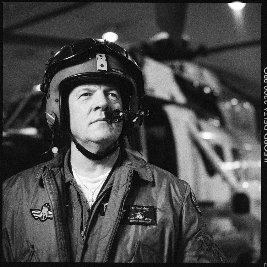 En person i flydrakt og hjelm står foran et helikopter og stirrer ettertenksomt ut i det fjerne. Foto: Nathan Lediard, Lediard Foto AS.