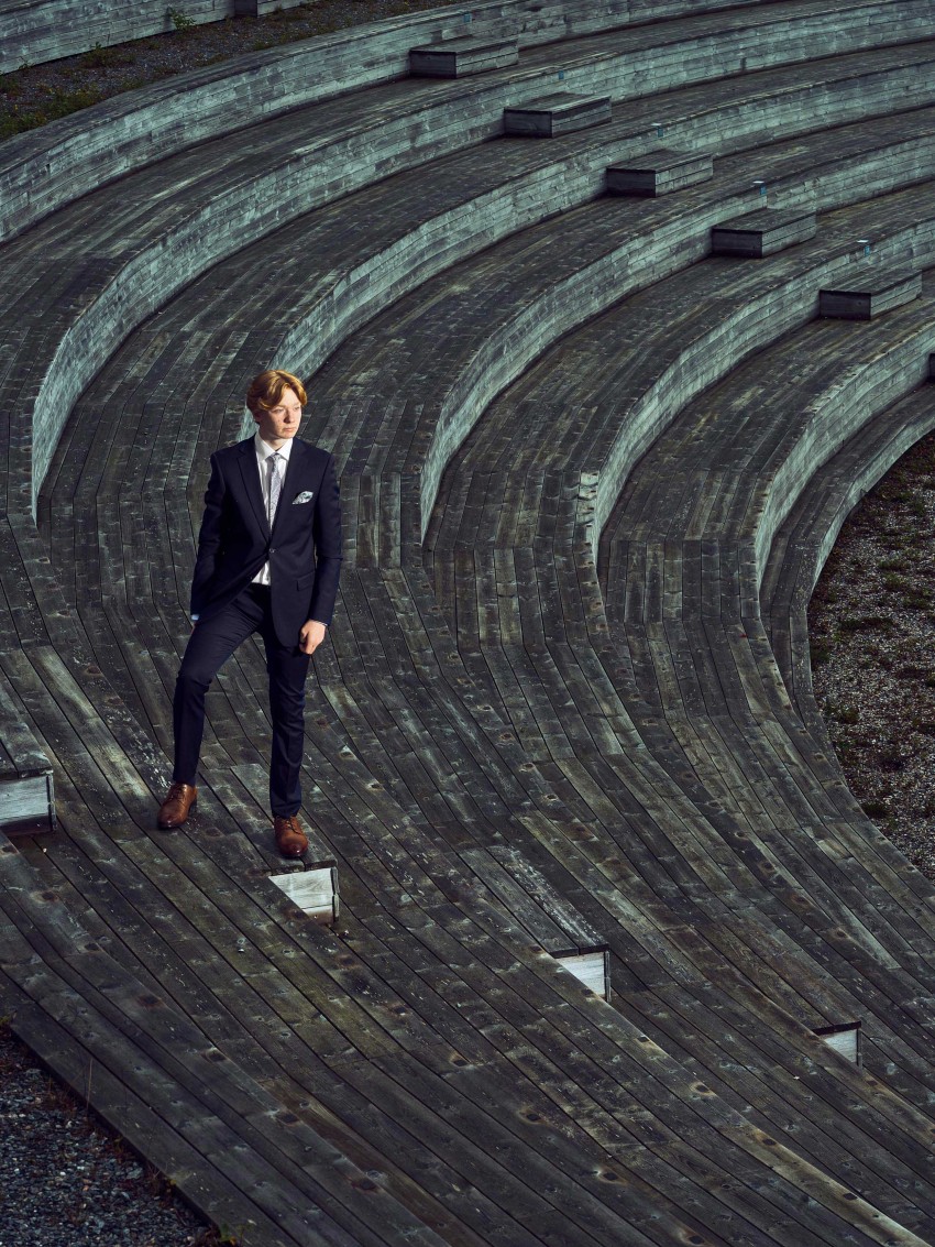 En person i dress står på en amfiteatertrapp i tre og ser opp, med et geometrisk mønster av linjer rundt. Foto: Nathan Lediard, Lediard Foto AS.
