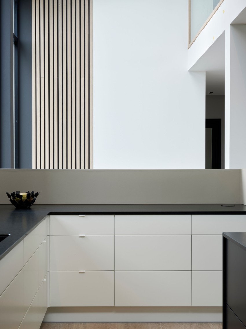 Minimalistisk kjøkken med hvite skap, svart benkeplate, en fruktskål og vertikale trelameller på veggen. Foto: Nathan Lediard, Lediard Foto AS.