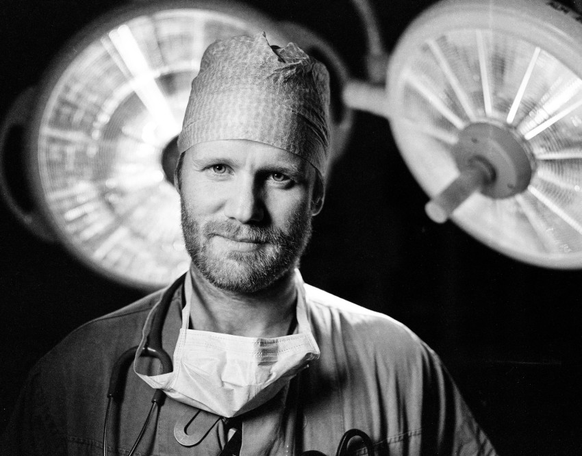 Mannlig lege i kirurgisk antrekk, inkludert maske og caps, står på en operasjonsstue med overlys. Foto: Nathan Lediard, Lediard Foto AS.