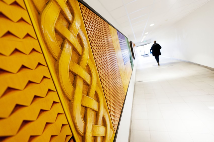 Gule geometriske og flettede mønstre på en vegg med en person som går nedover gangen i bakgrunnen. Foto: Nathan Lediard, Lediard Foto AS.