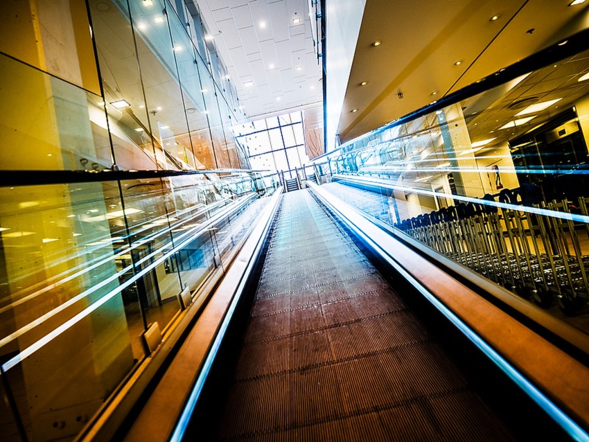 Vidvinkelvisning av en bevegelig gangvei i et moderne, godt opplyst, glassforet bygningsinteriør. Foto: Nathan Lediard, Lediard Foto AS.