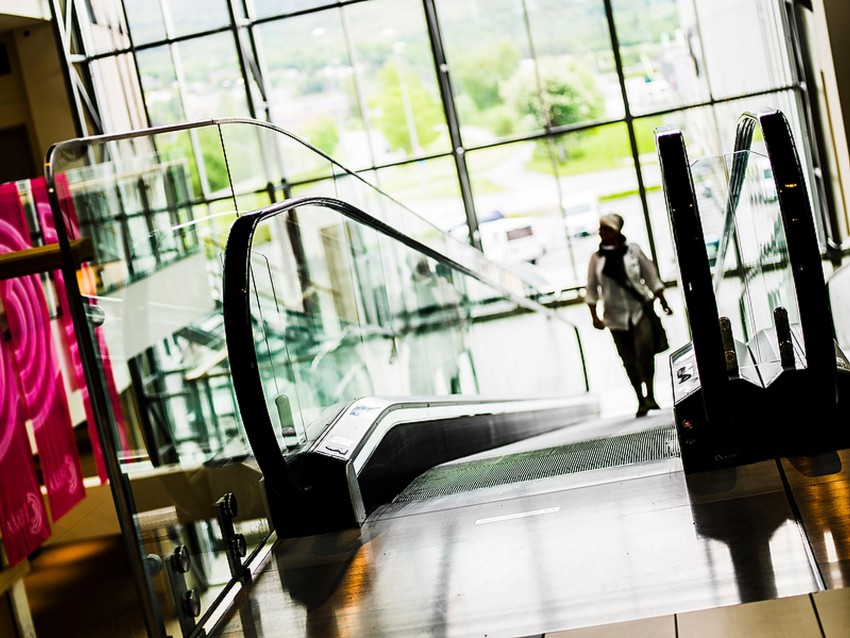 Ser ned en rulletrapp i en lys bygning med en silhuett av en person i det fjerne. Foto: Nathan Lediard, Lediard Foto AS.