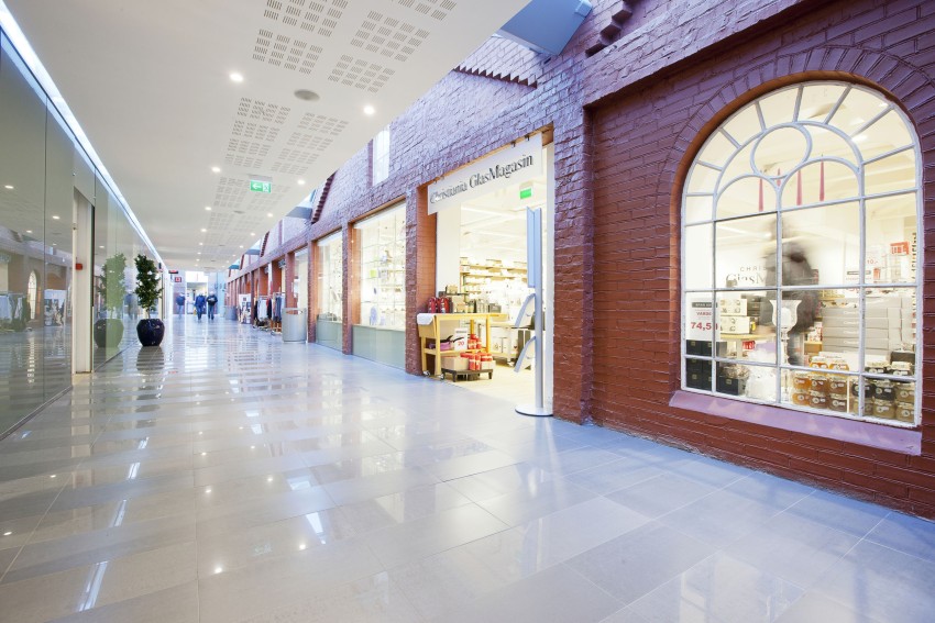 Lys kjøpesenterkorridor med murvegger, buede vinduer og en butikk på høyre side. Foto: Nathan Lediard, Lediard Foto AS.